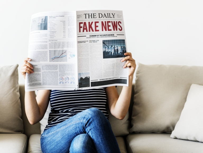 Woman reading newspaper that says 'Fake News'