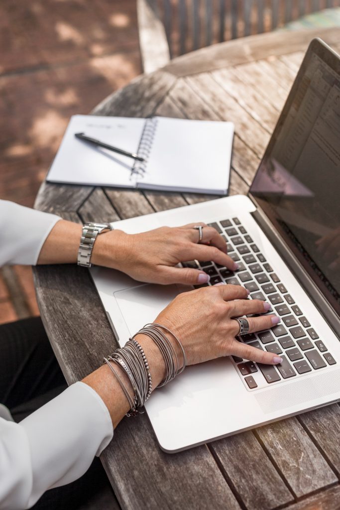 Hands typing on laptop next to notepad