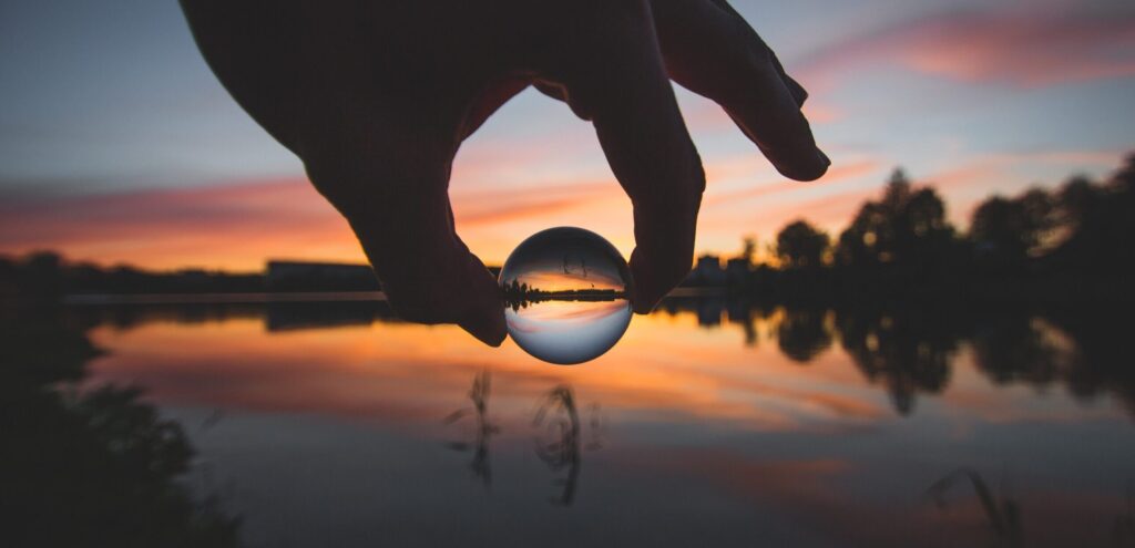 Hand holding glass ball against a sunset