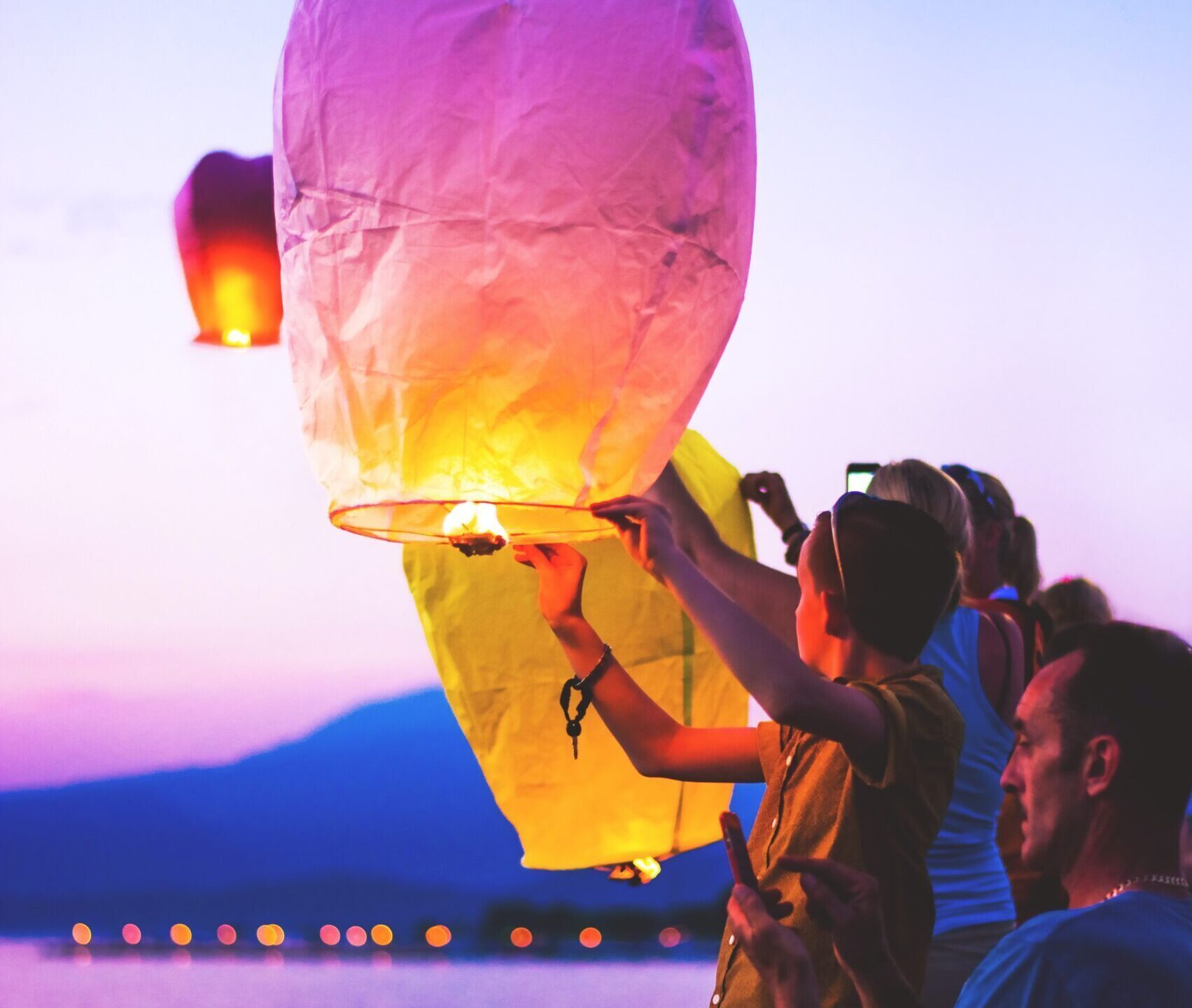 People holding up a sunset-coloured balloon-shaped lantern in the evening.
