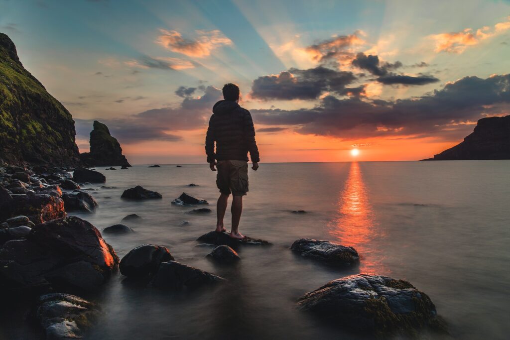 Man standing on a rock by the sea looking out onto sunset