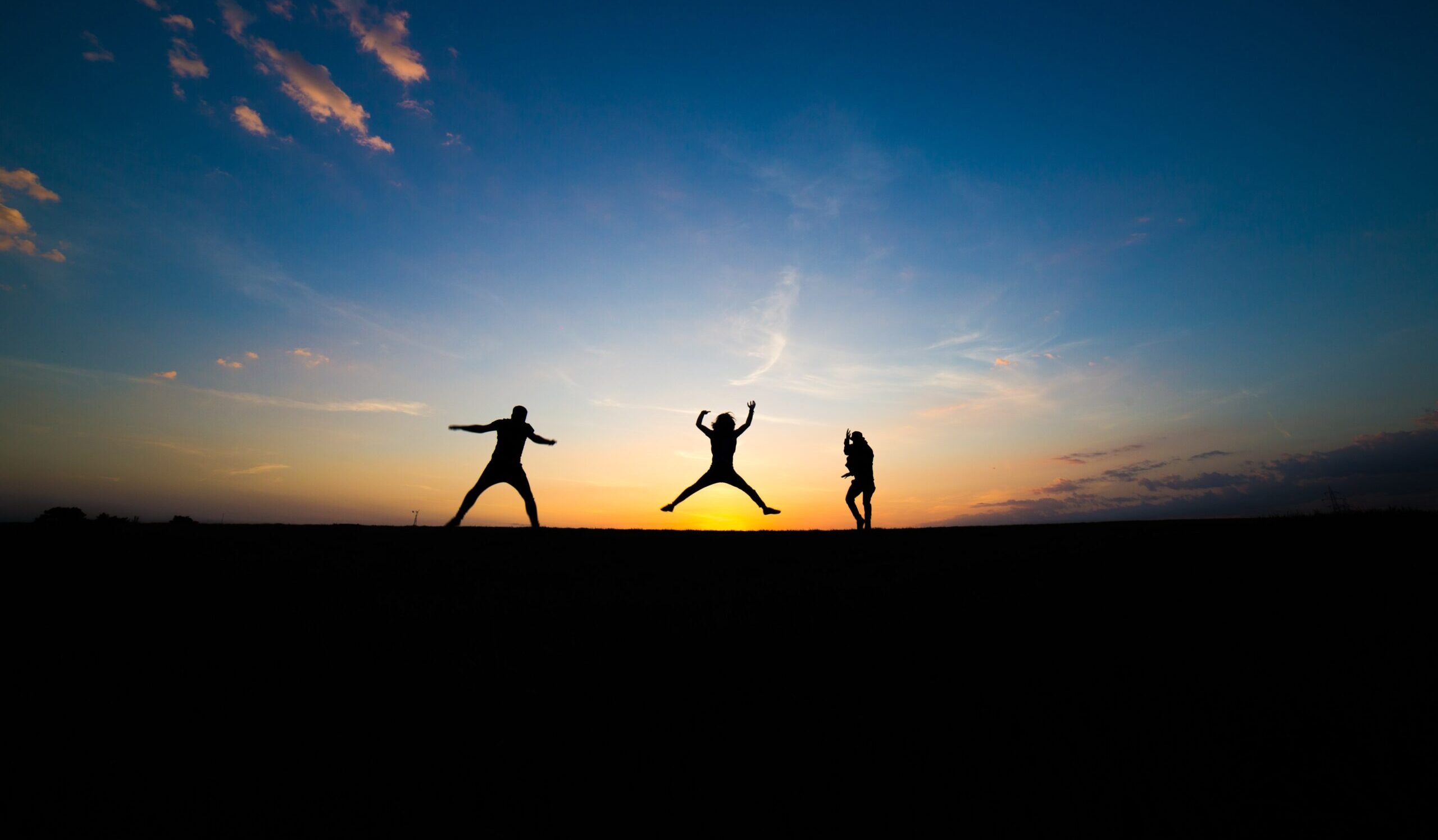 Three silhouettes of people jumping against a dark background with sunset