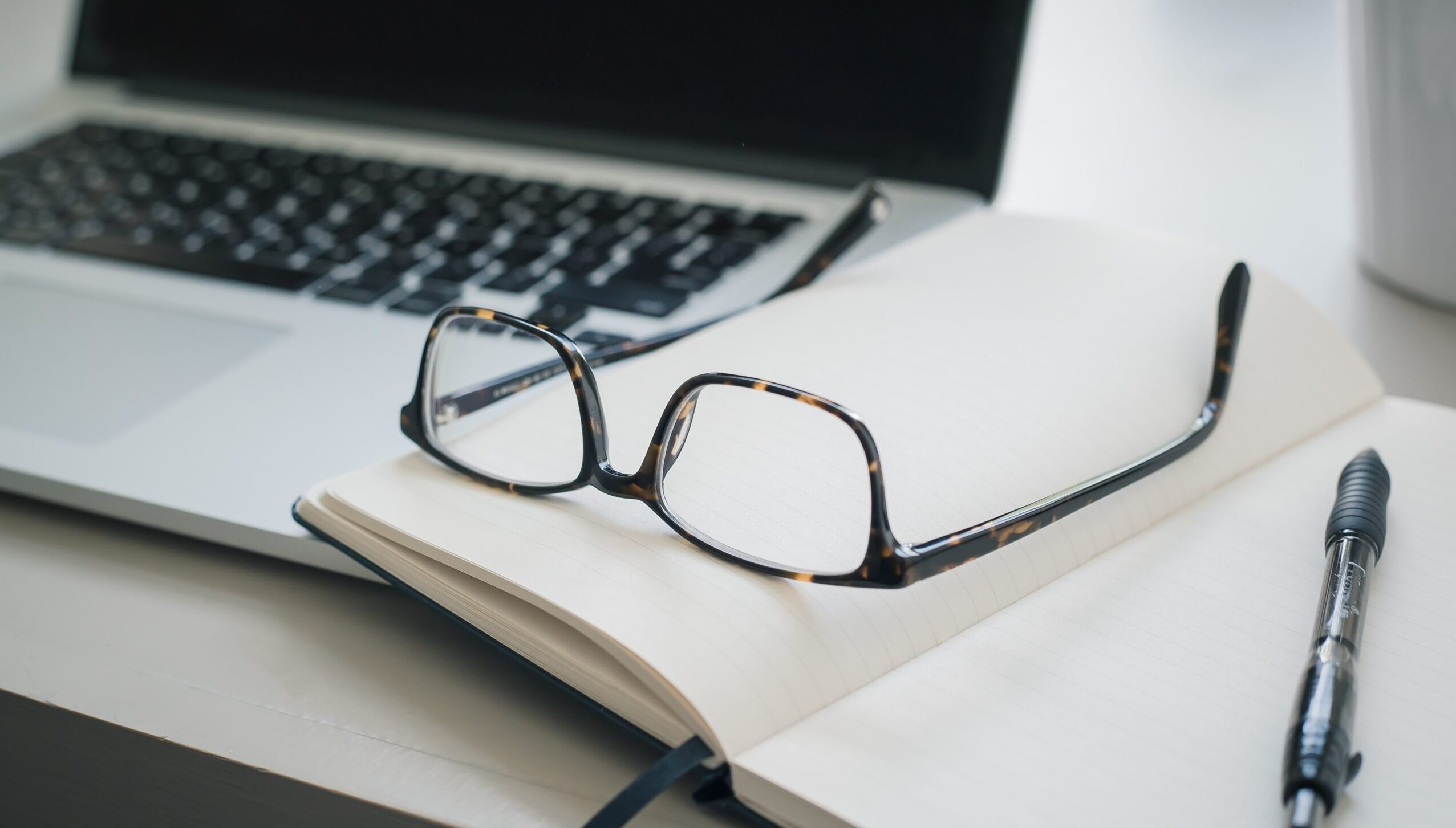 Glasses on top of notepad next to laptop